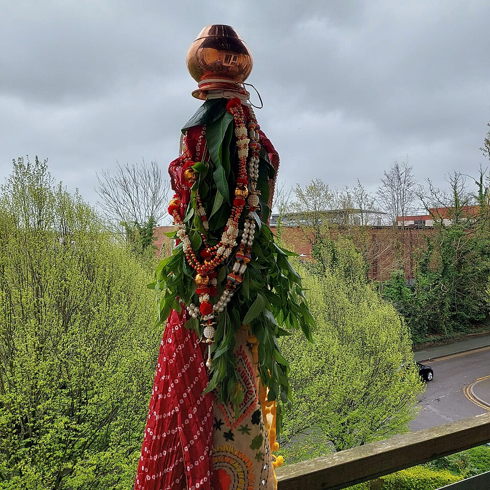 A gudi with cloth, garlands and a vessel, displayed outside a home